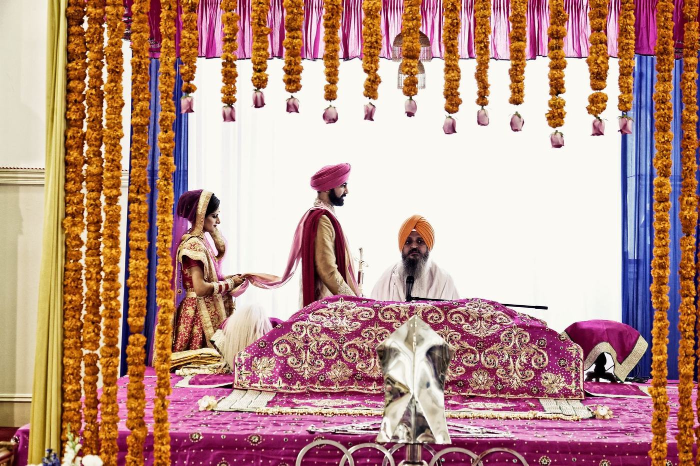 Anand Karaj ceremony before the Guru Granth Sahib beneath marigold garlands