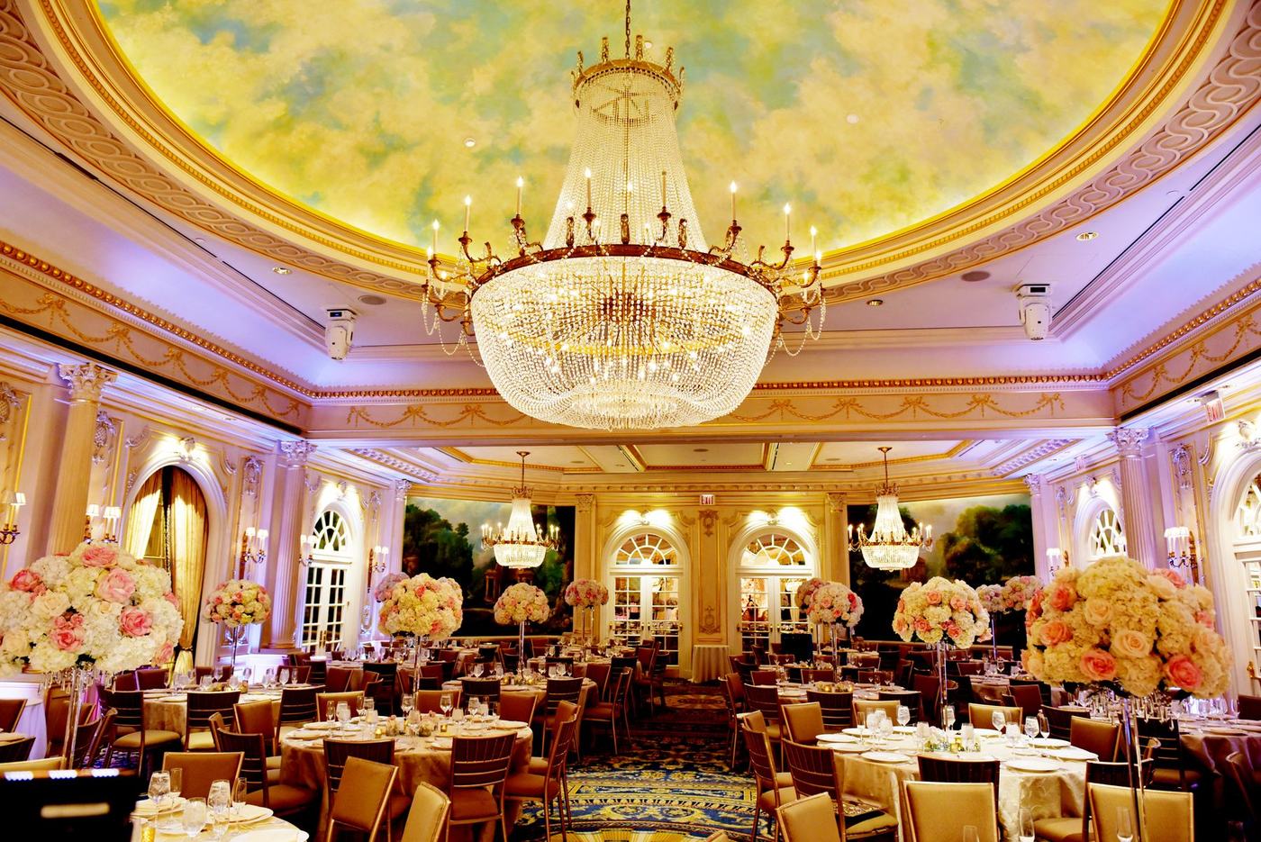 Ballroom with a painted sky ceiling, chandeliers and floral tables
