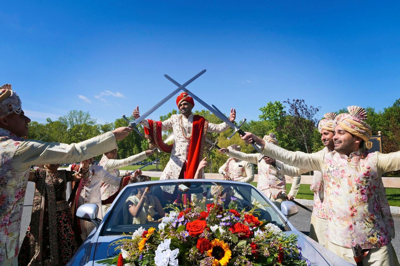 Swords raised over the groom's flower-covered convertible as the baraat begins