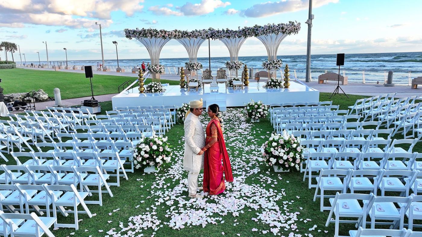 Beach ceremony aisle of white chairs and petals leading to the mandap