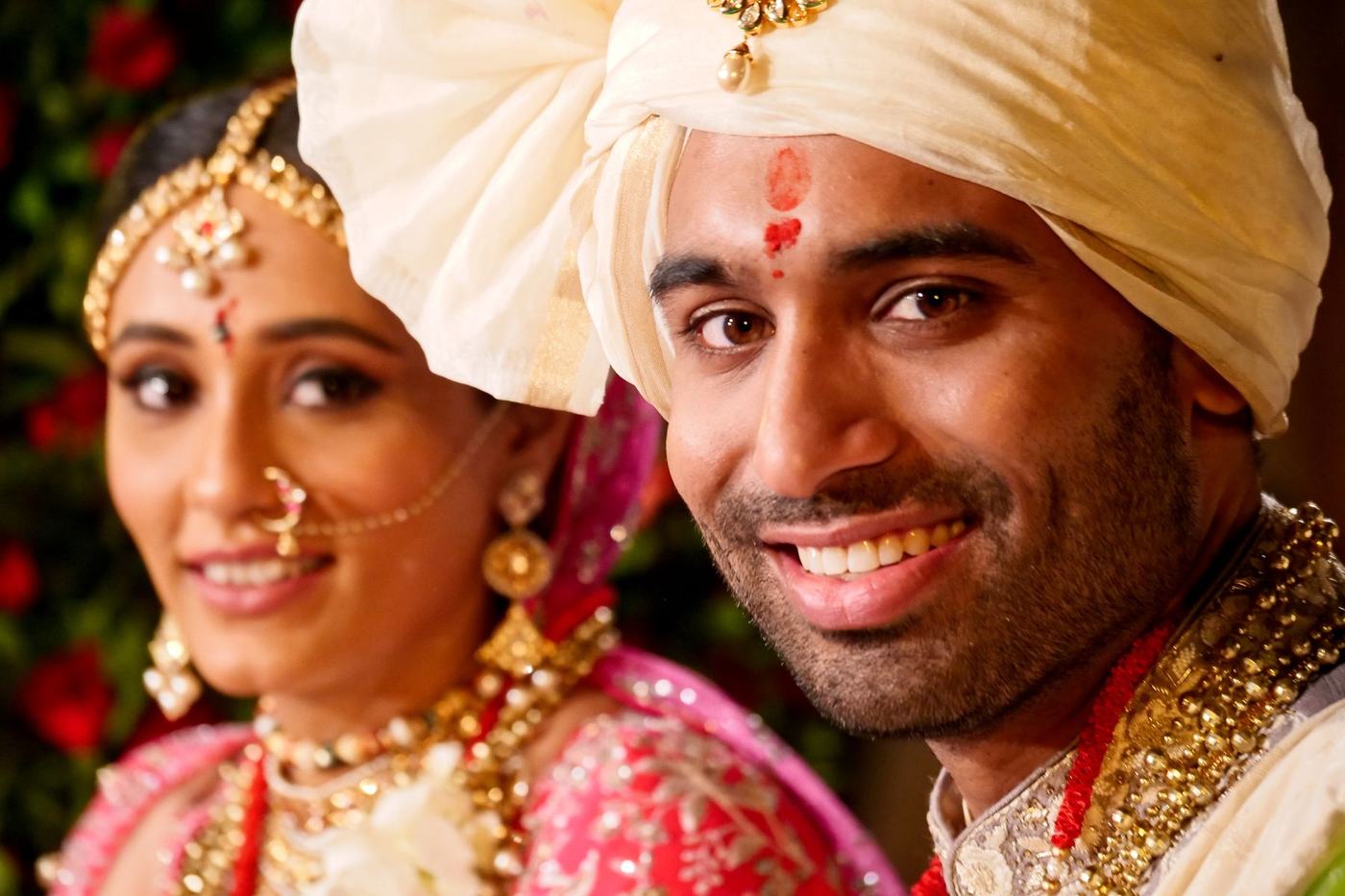 Bride in red and groom in a cream safa smiling together after the ceremony