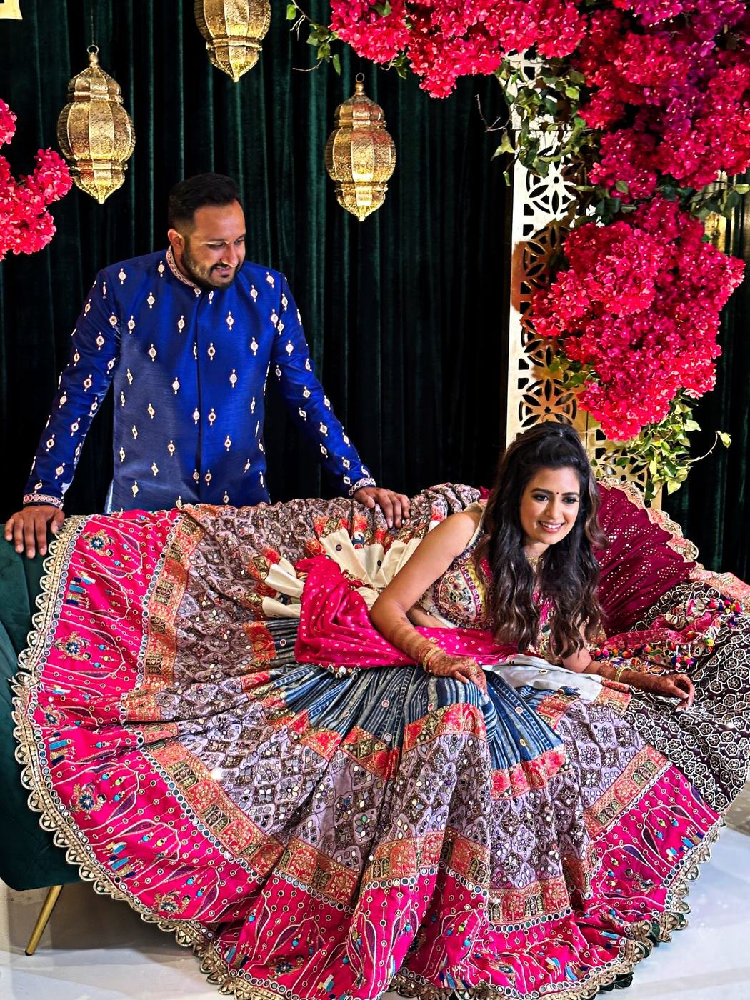 Bride fanning out her multicoloured embroidered lehenga beneath pink bougainvillea