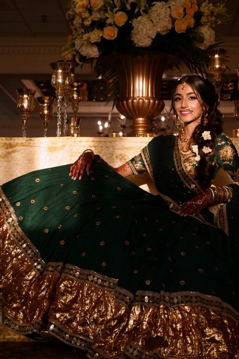 Bride in emerald and gold fanning out her lehenga in candlelight