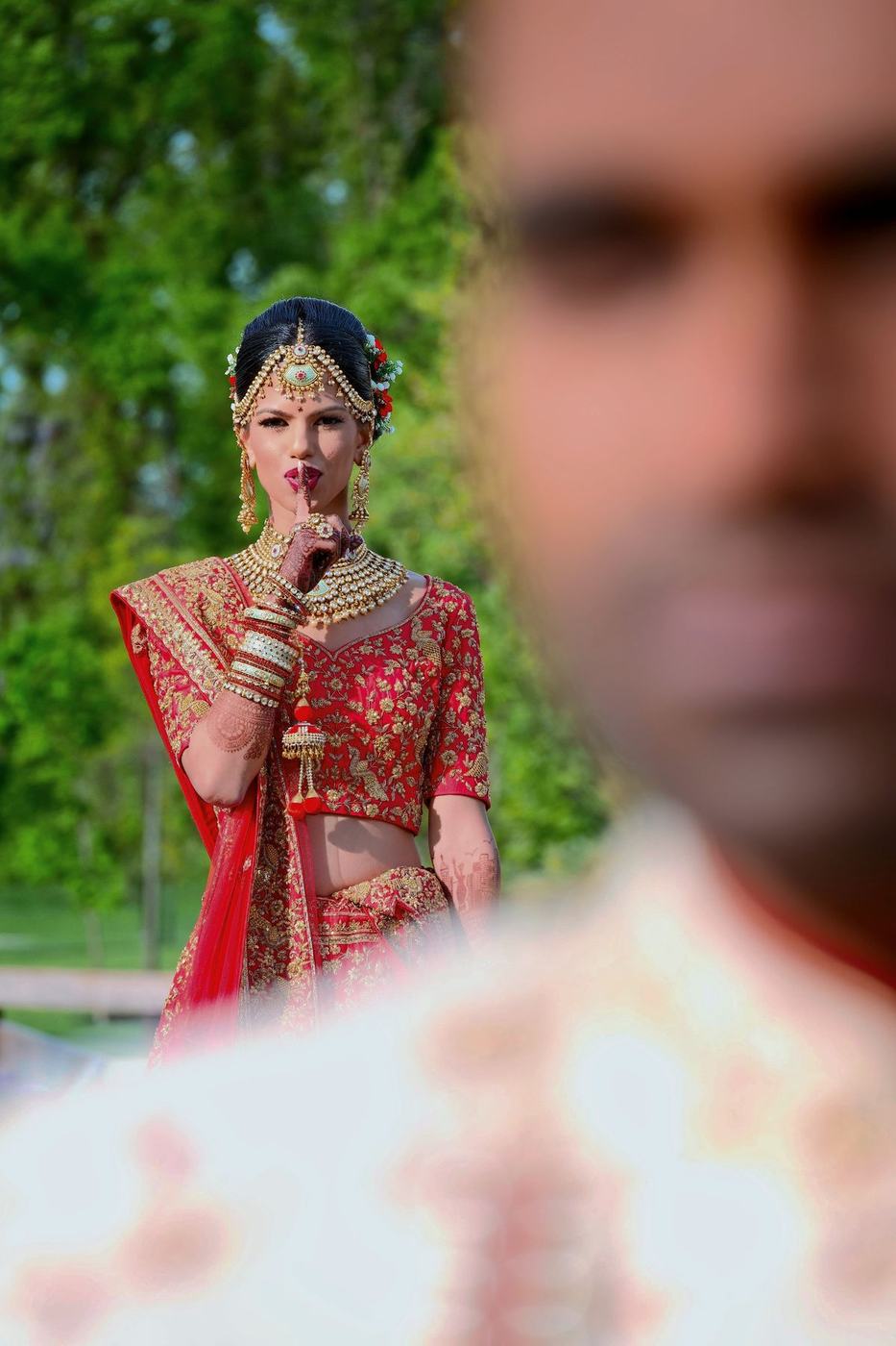Bride in red seen past the groom's shoulder, finger to her lips