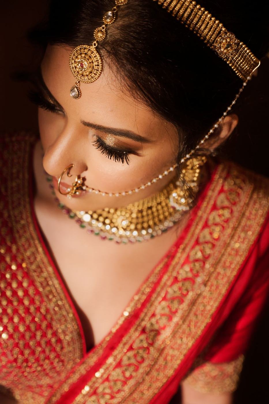 Bride in red with a gold nath and jhumkas, eyes lowered