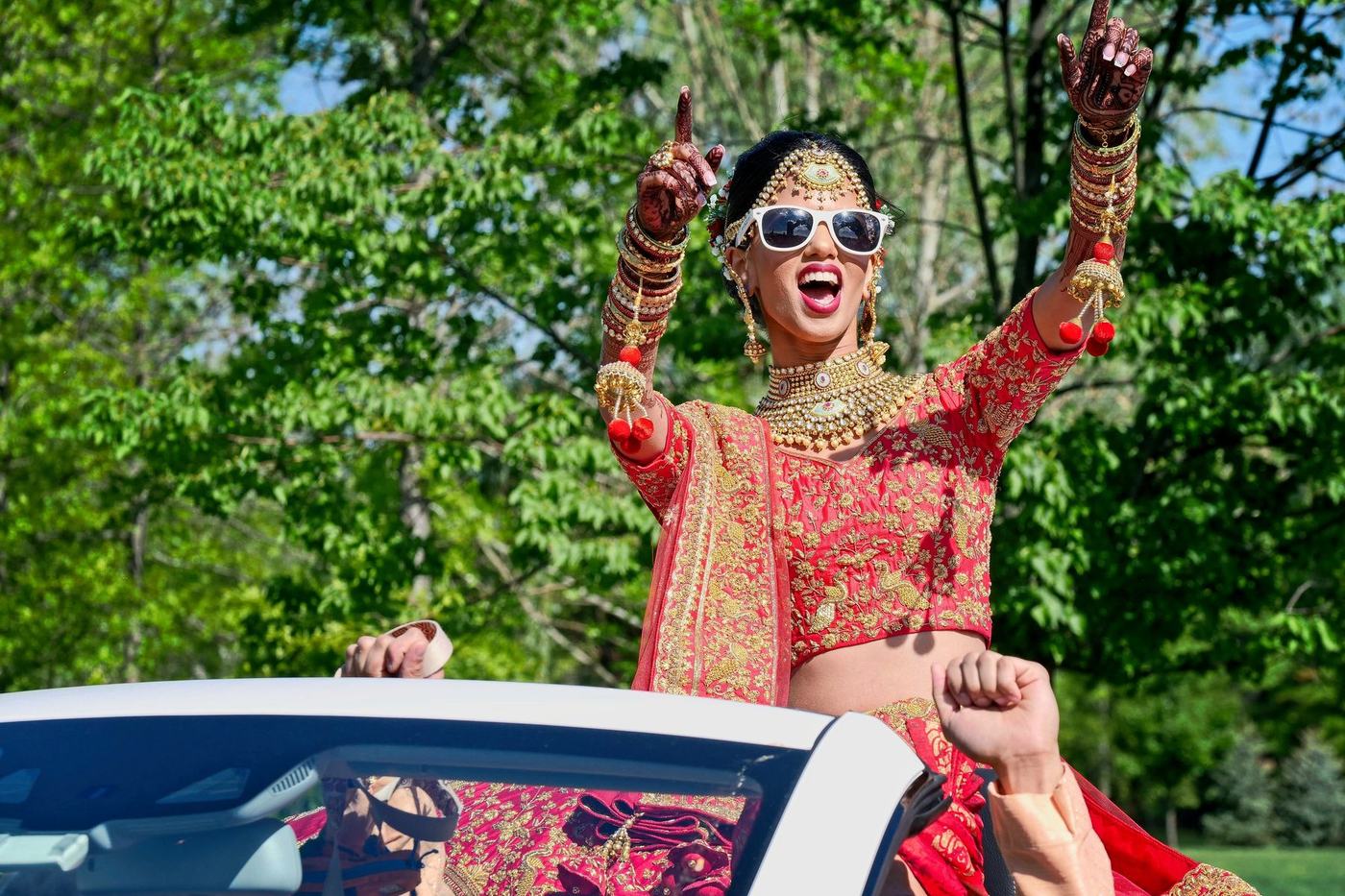 Bride in sunglasses cheering from the back of a white convertible