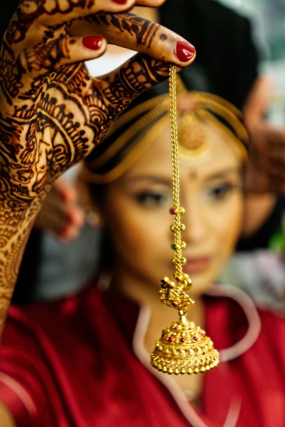 Bride lifting a gold jhumka to her ear, mehndi on her hands