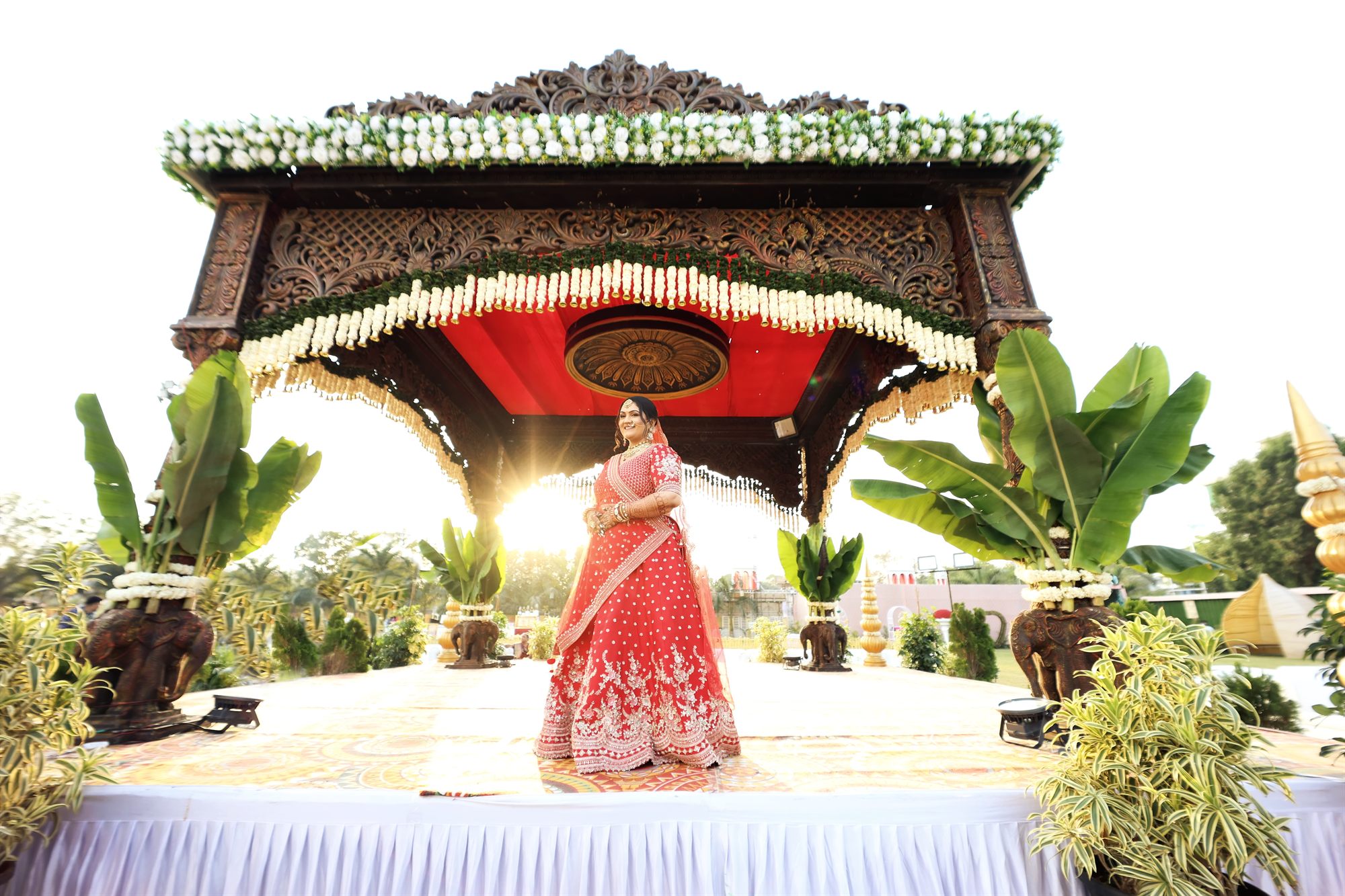 Bride standing beneath the mandap as sunlight breaks through behind her
