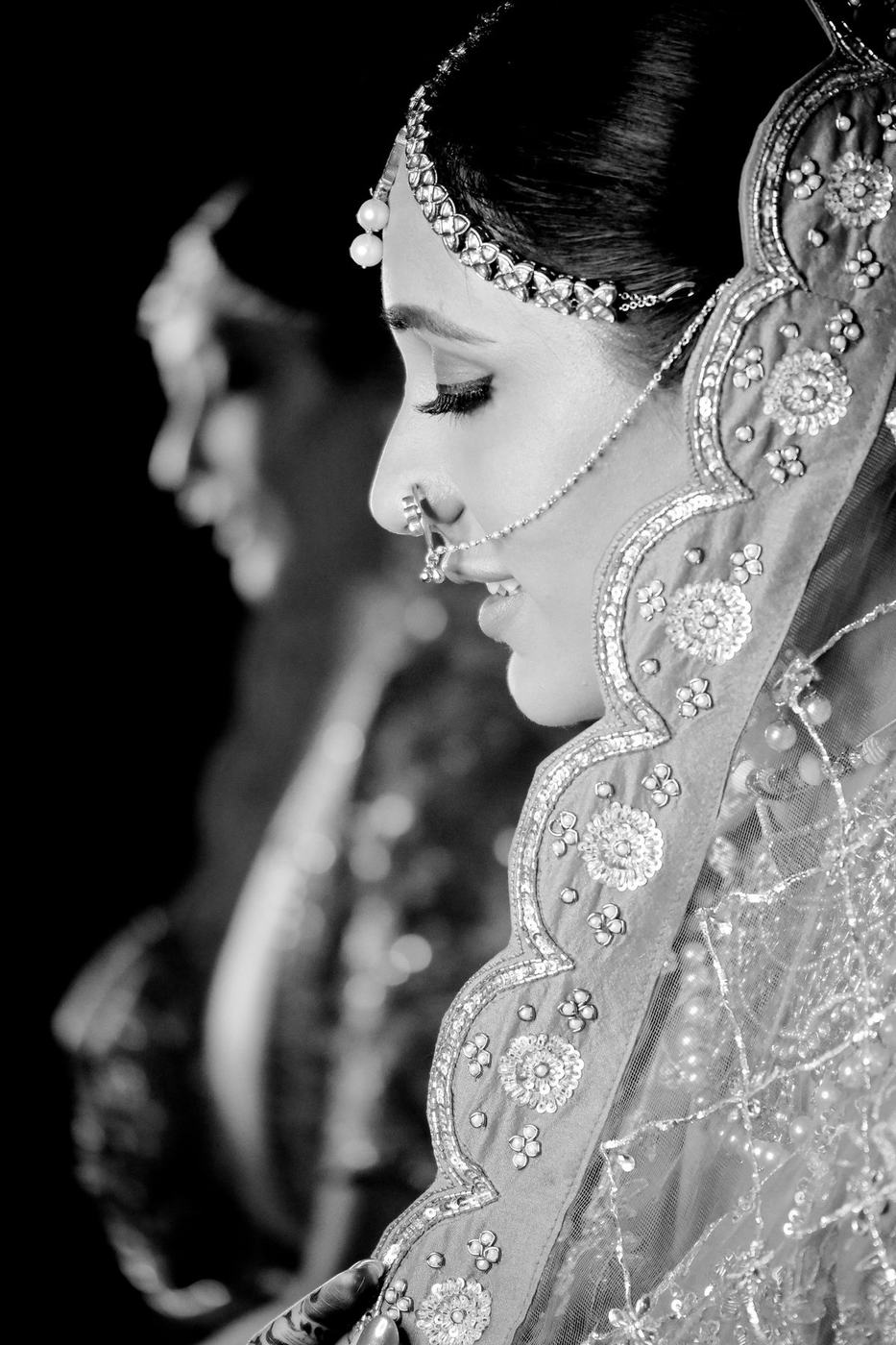Bride in profile under an embroidered dupatta, in black and white