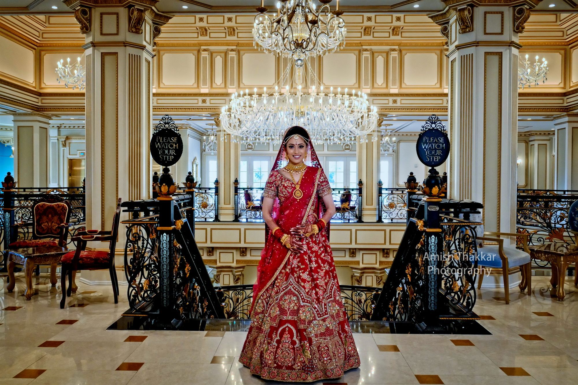 Bride in red pausing on a marble staircase inside a gilded hotel lobby