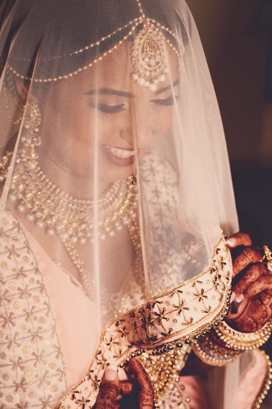 Bride smiling down beneath her embroidered veil