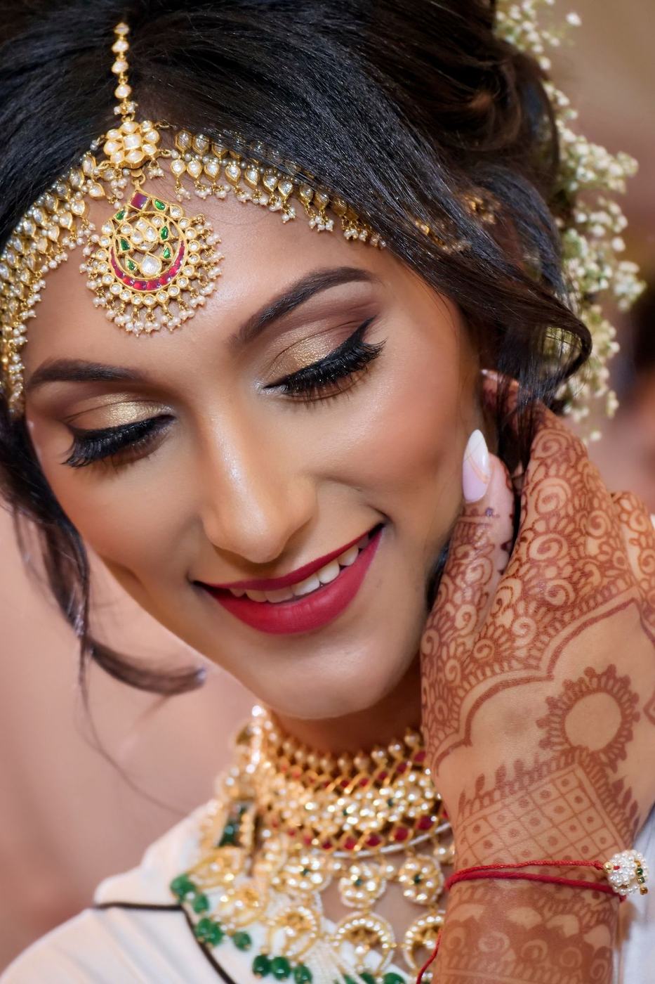 Bride smiling down with mehndi hands and emerald jewels