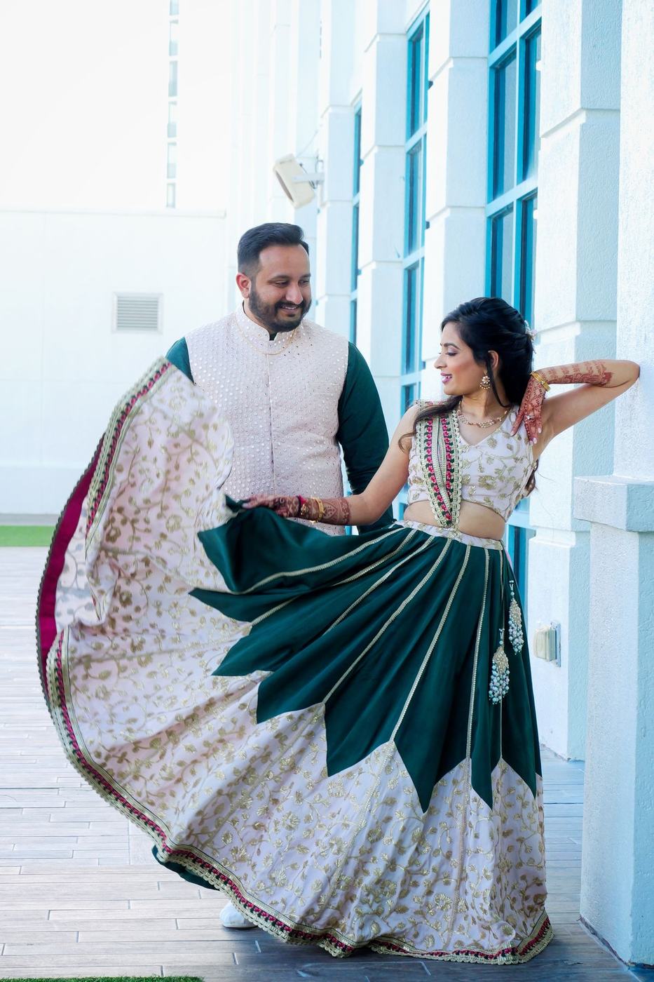 Bride spinning in green and white beside tall windows, groom watching