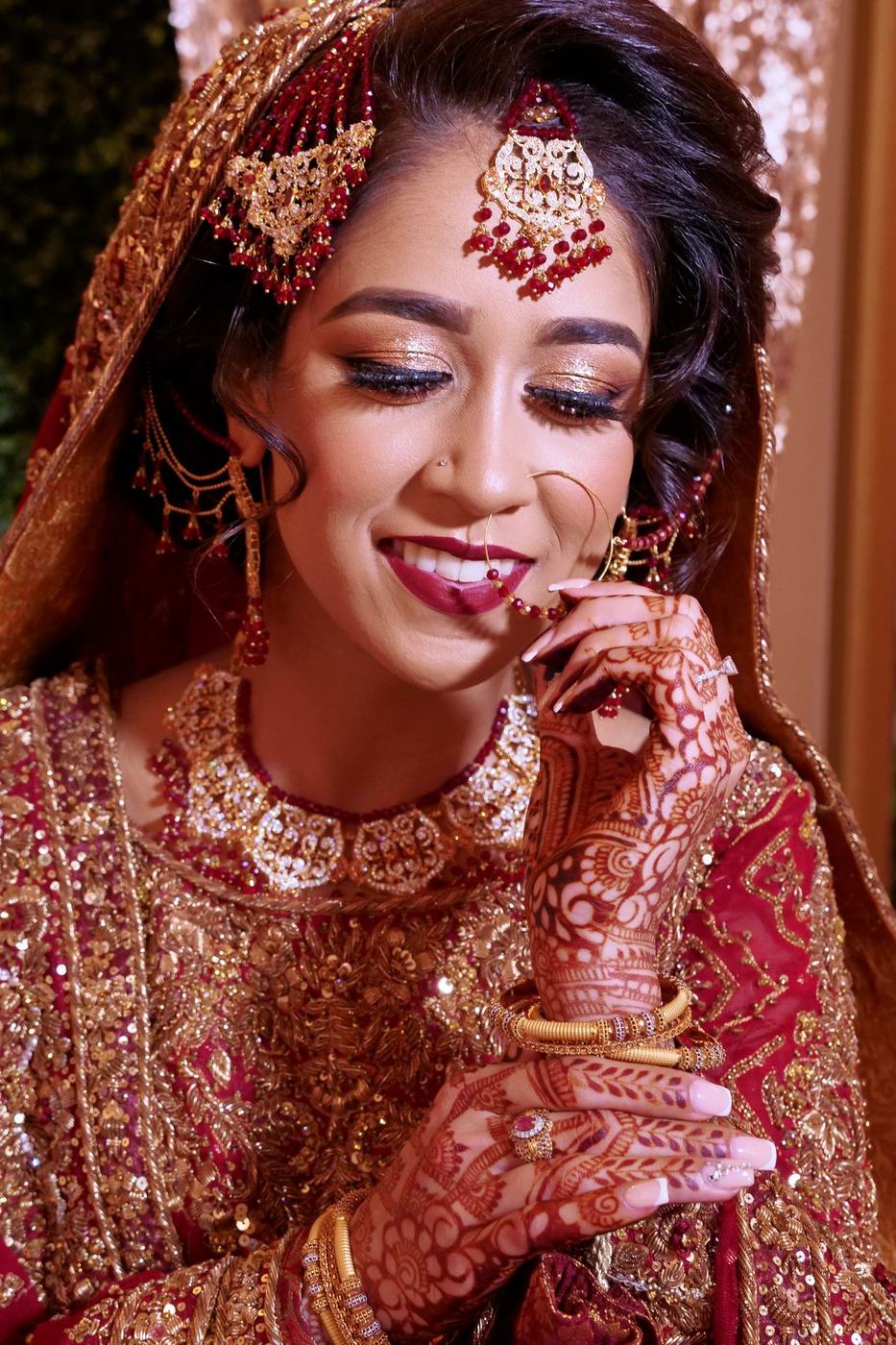 Bride with mehndi hands at her chin, red and gold jewels