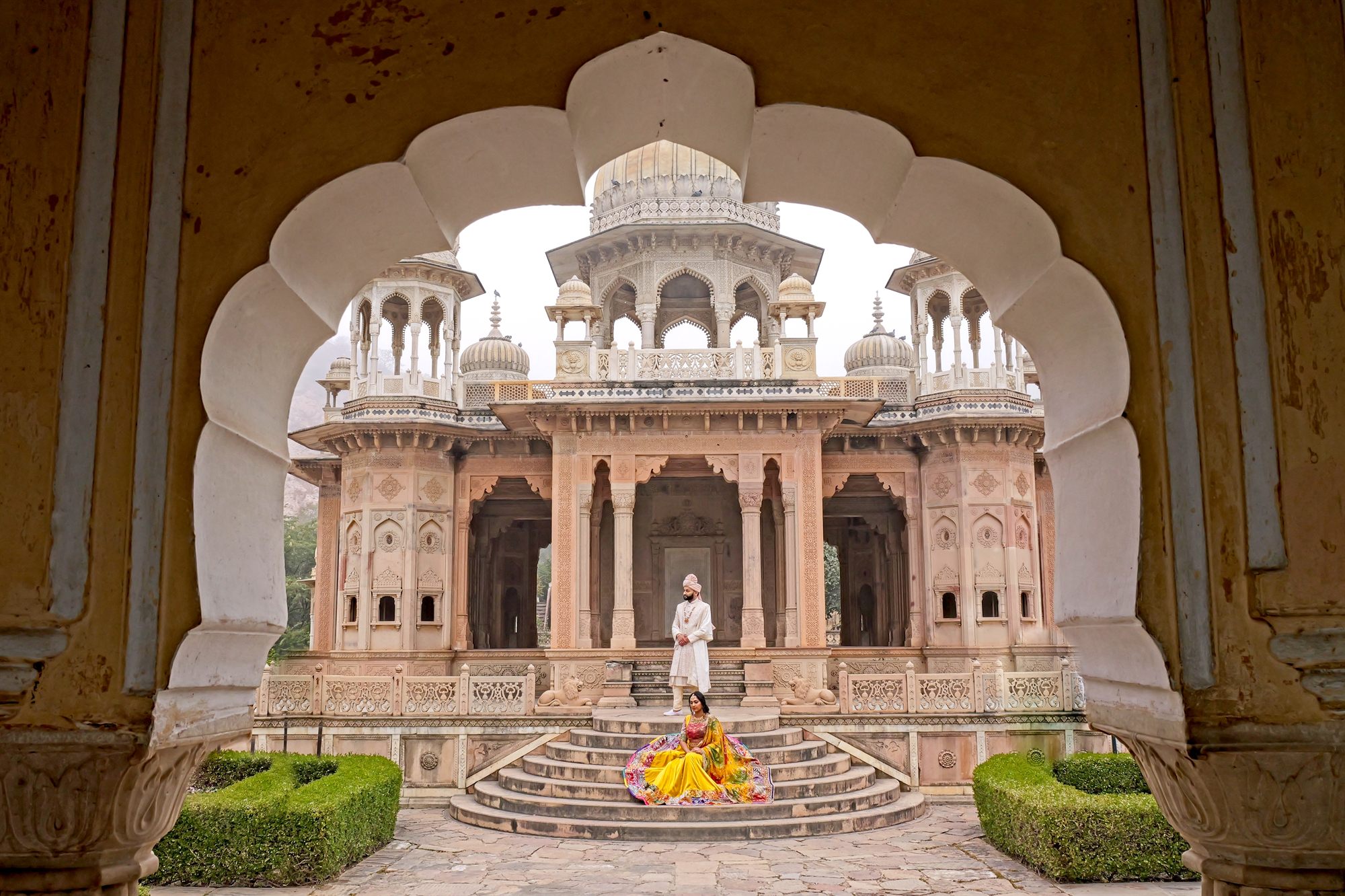 Bride in yellow framed by the carved arches of a palace pavilion