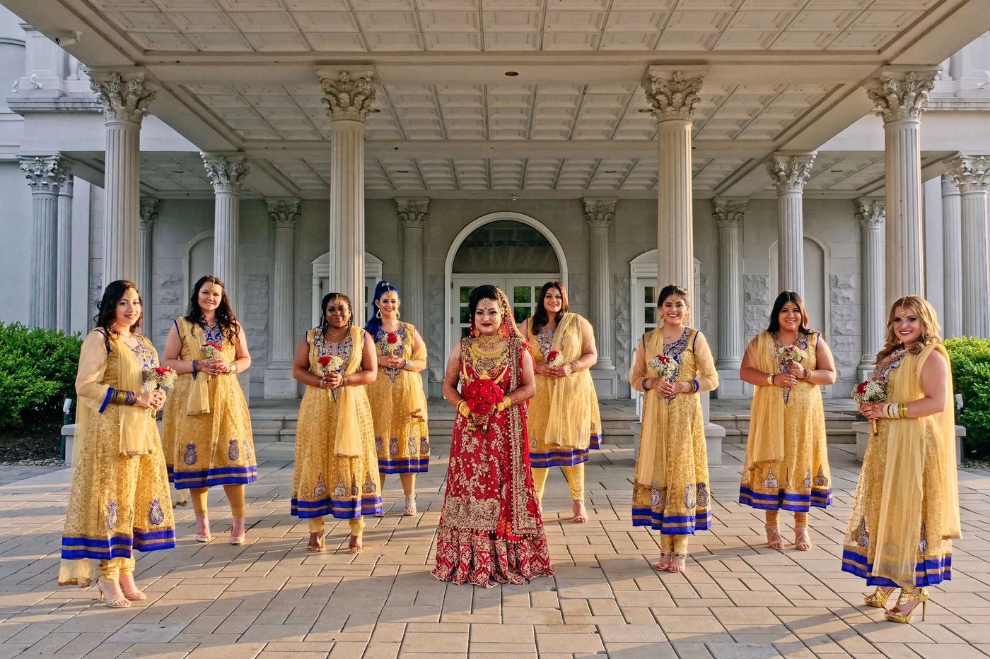 Bride with her bridesmaids in gold along a white colonnade