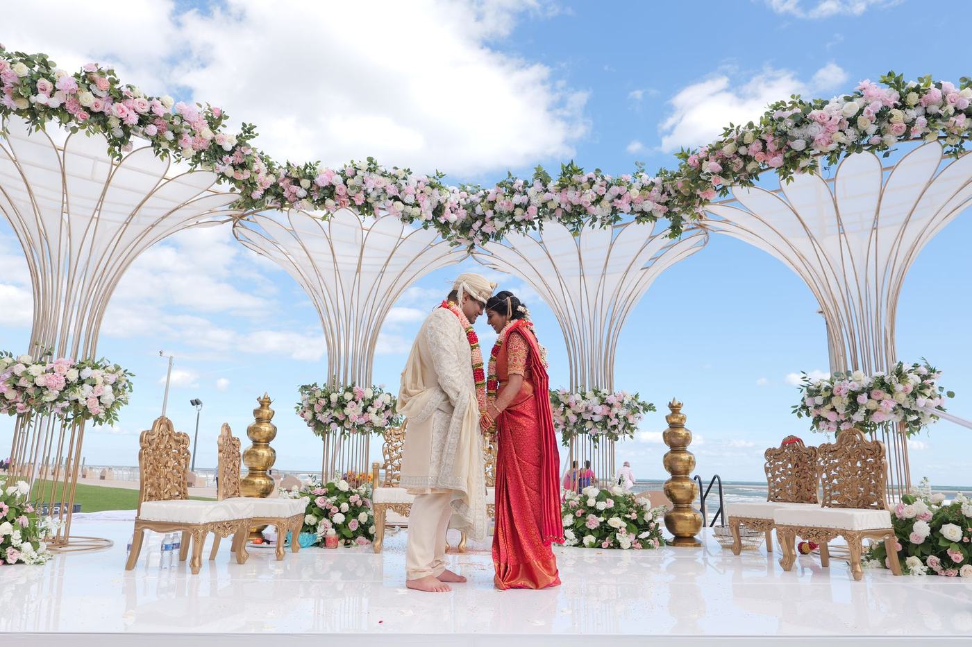 Couple at the white beach mandap under a blue sky
