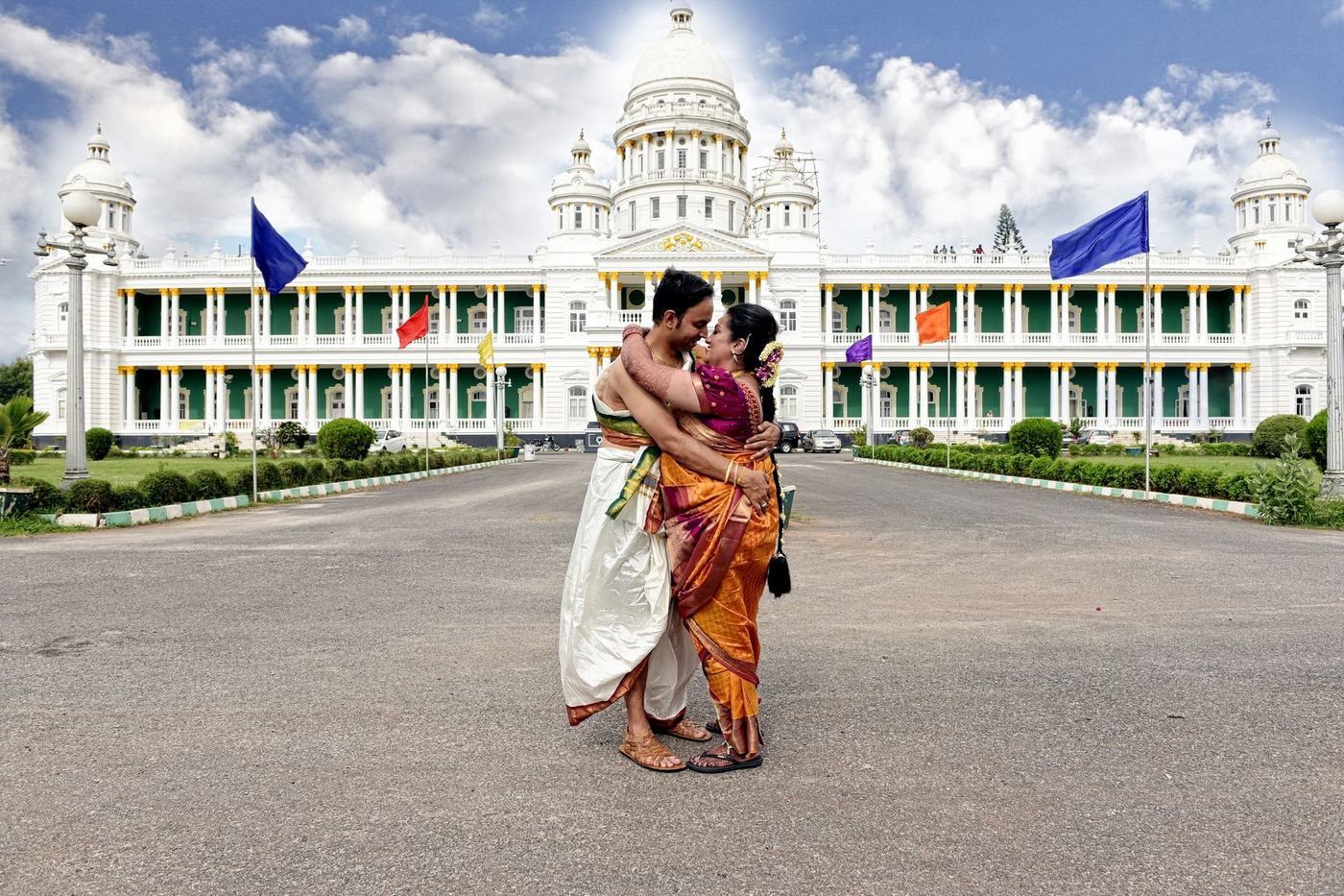 South Indian couple before a white palace facade under monsoon clouds