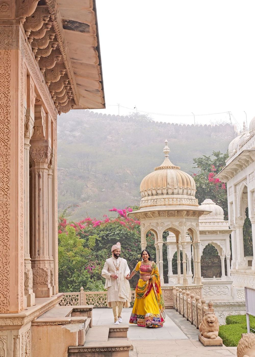 Couple standing between marble chhatris with the Rajasthan hills behind them