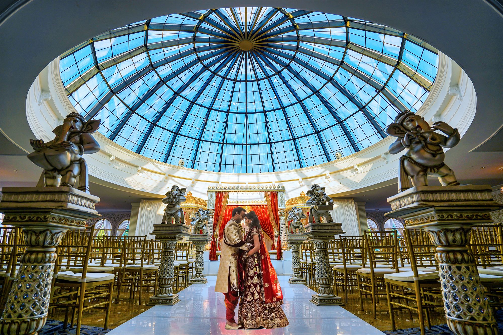 A couple standing quietly together beneath a domed ballroom ceiling before the ceremony begins