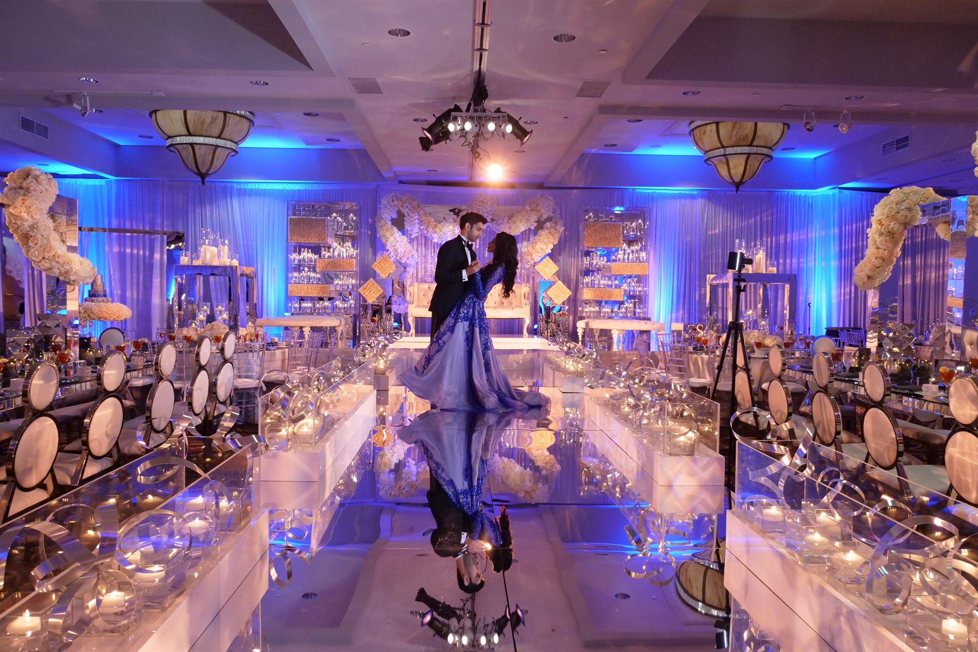 Couple dancing alone on a mirrored floor beneath blue reception light
