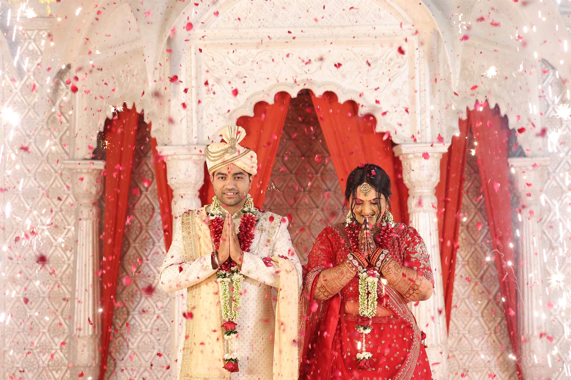 Couple exchanging garlands as petals fall around them