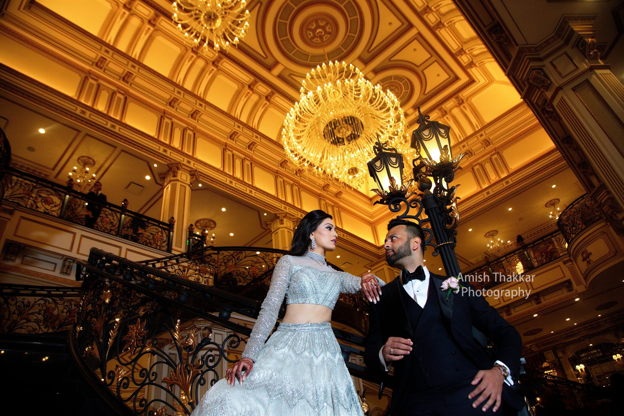 Couple pausing on a gilded staircase beneath ballroom chandeliers