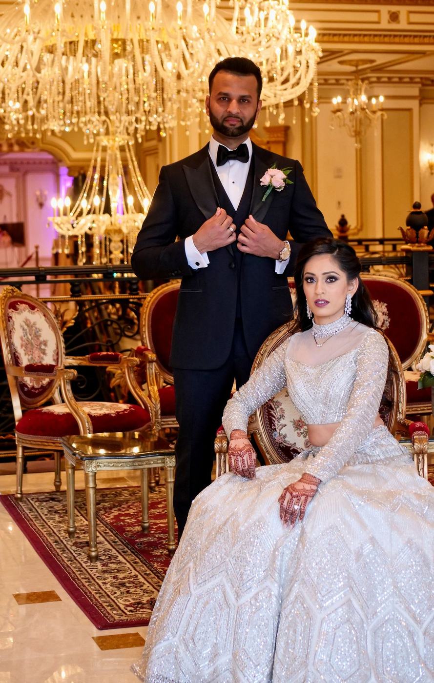 Couple in silver and black on gilded chairs beneath a chandelier