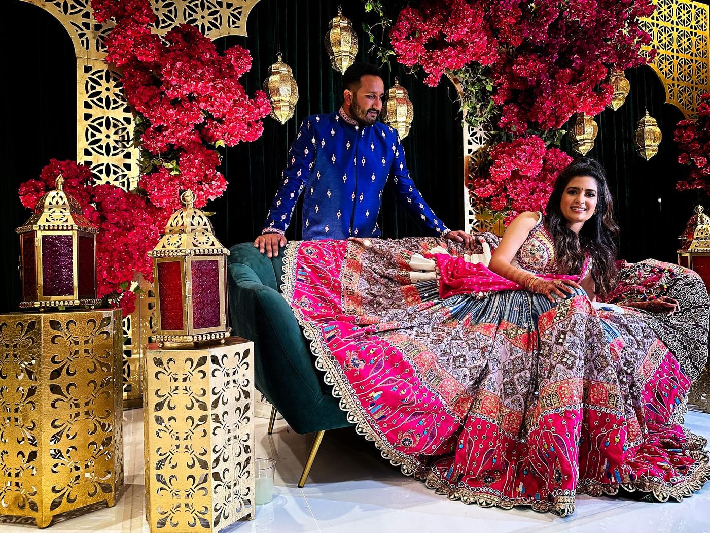 Couple on the sangeet stage between brass lanterns and pink bougainvillea