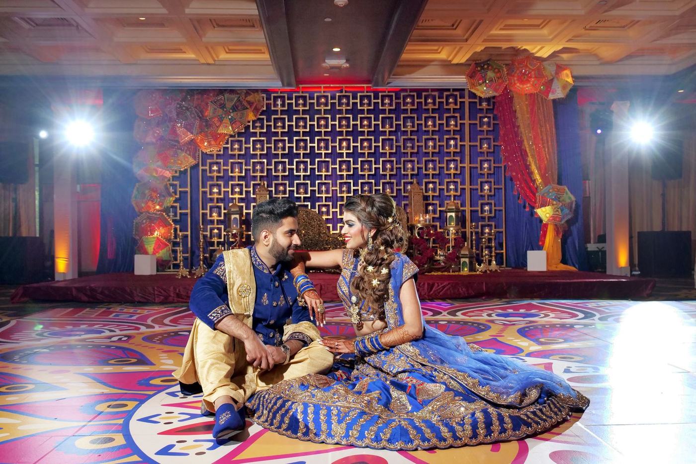 Couple seated on the painted sangeet floor in blue and gold