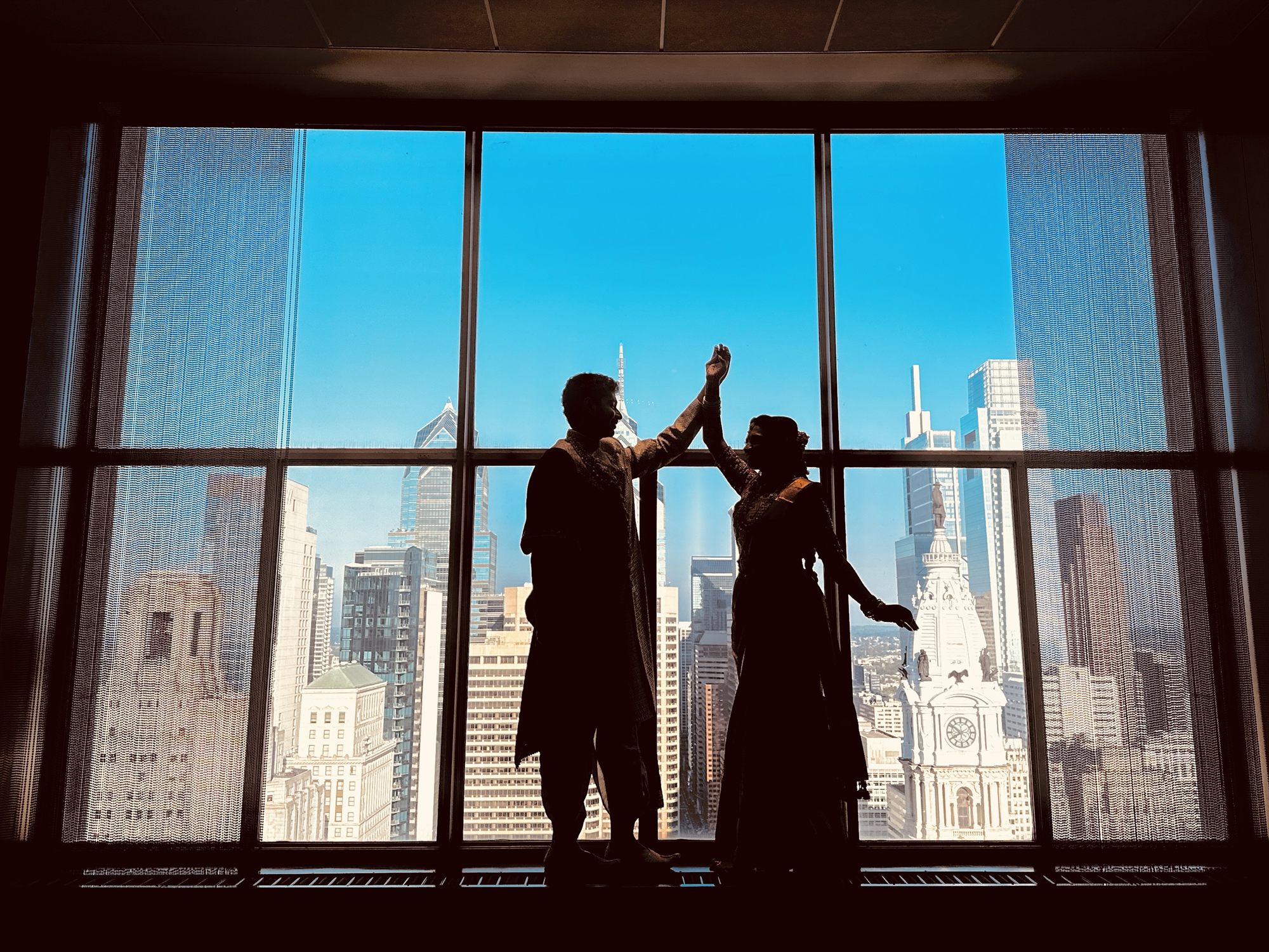 Couple silhouetted against a city skyline through a tall window at the end of the night