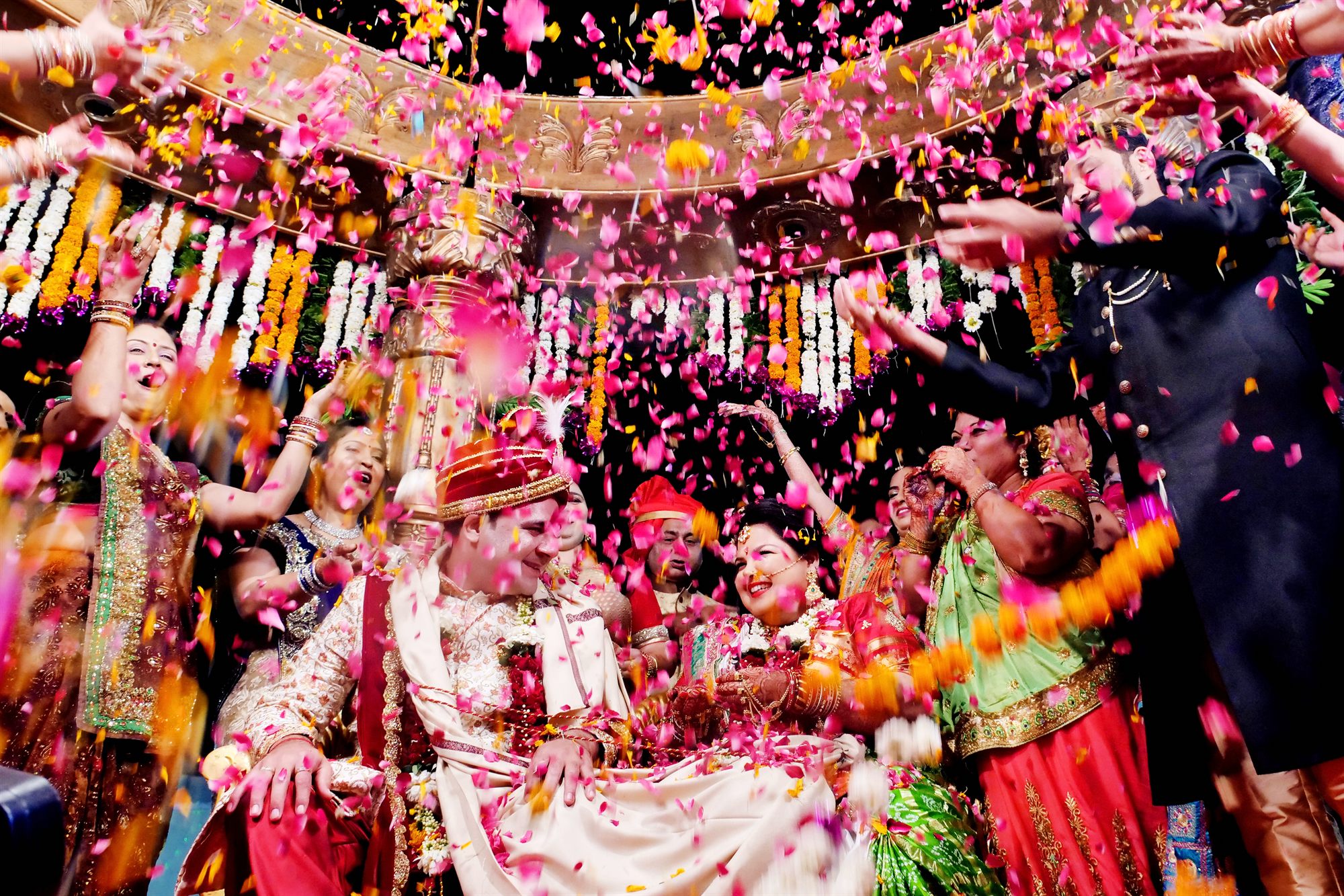 Family surrounding the couple with marigold petals as the procession arrives
