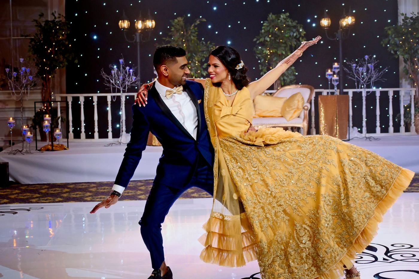 First dance dip, the bride in a gold lehenga on a white dance floor