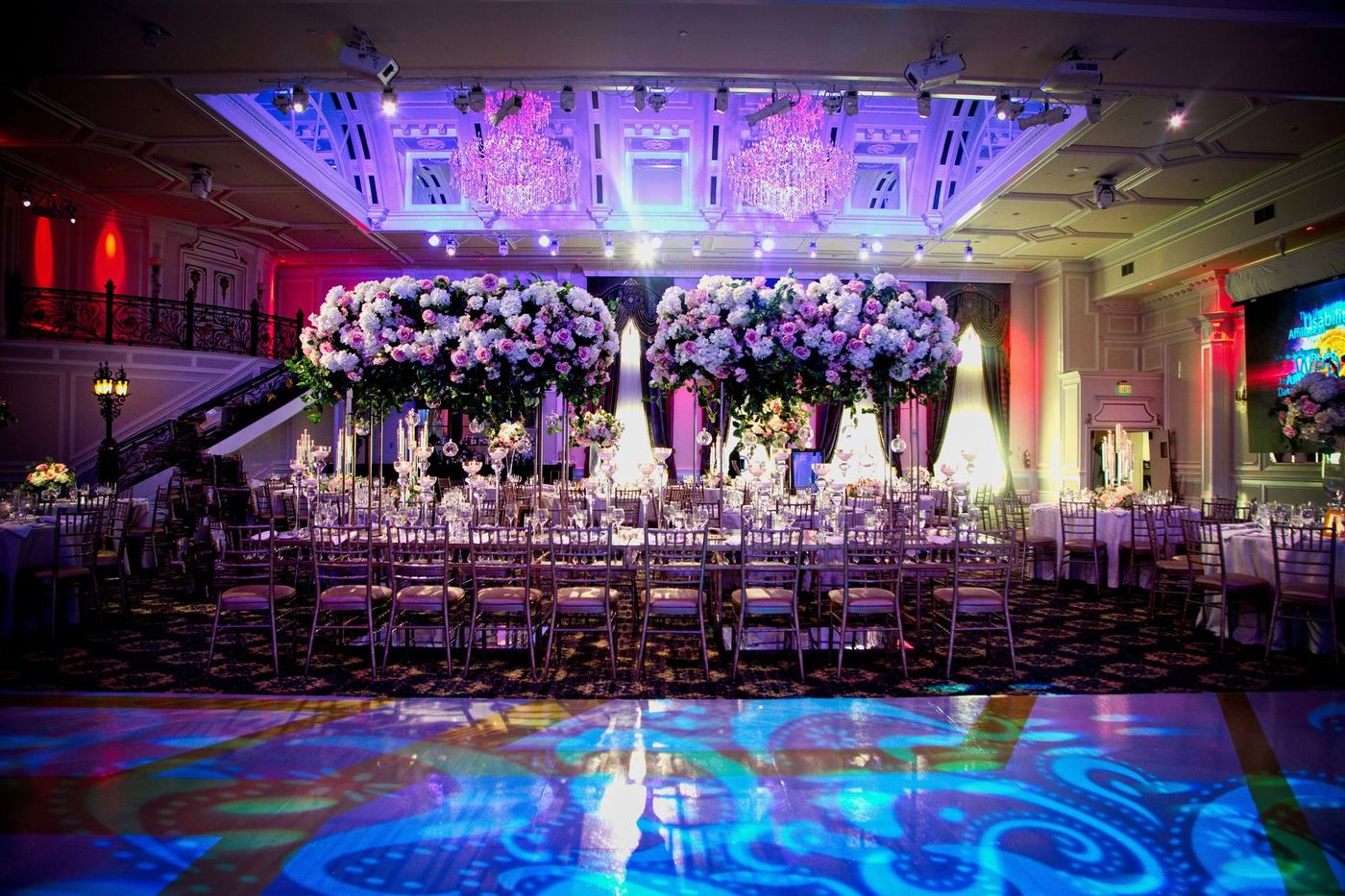 Grand ballroom in purple and blue light with a floral stage and full tables