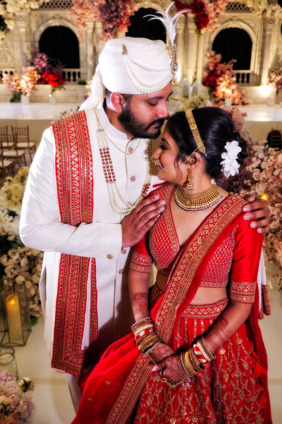 Groom in ivory and red holding the bride close among florals