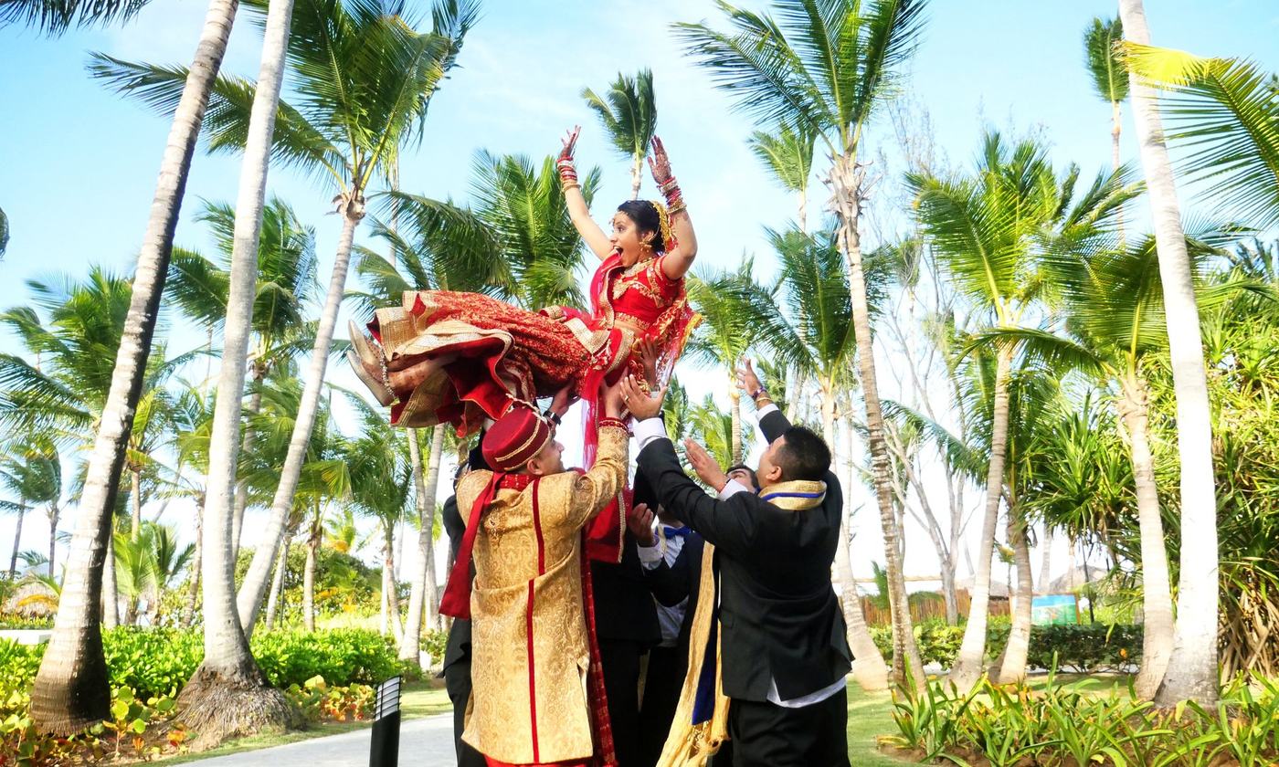 Groom lifted high in the baraat under the palms