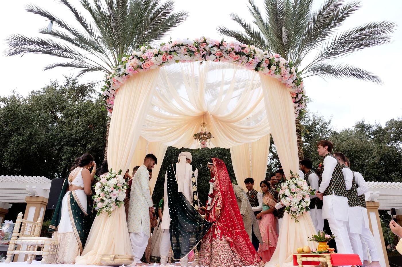 Open-air mandap beneath tall palms, the couple seated inside