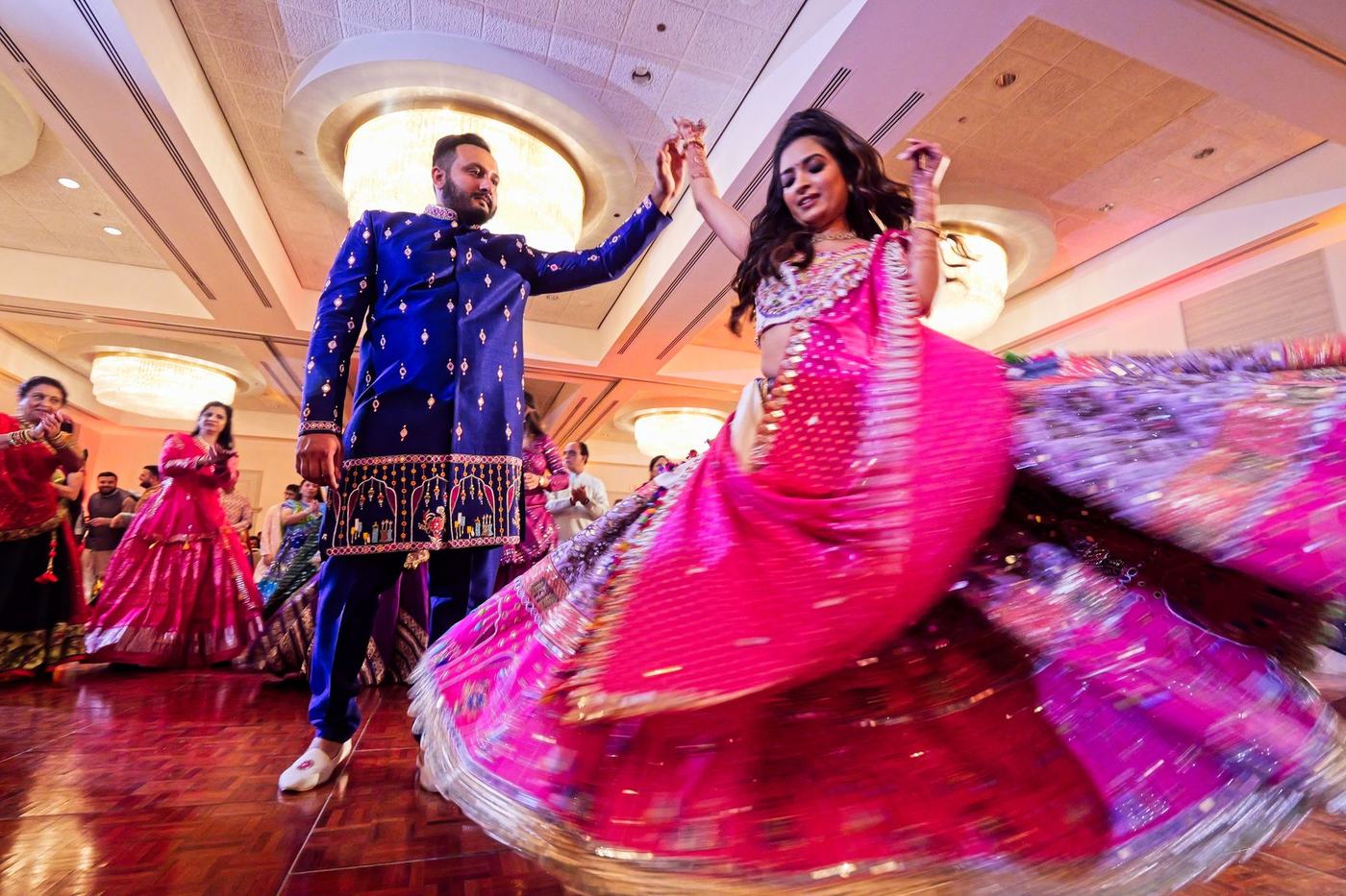 Bride's pink lehenga spinning beside the groom in blue at the sangeet
