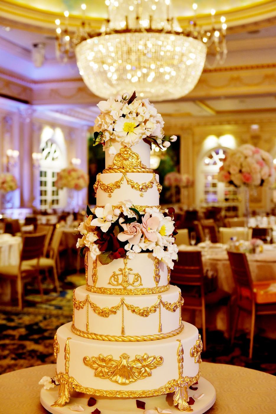 Tiered white and gold wedding cake beneath the chandelier